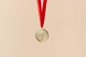 Close-up of a gold medal with a red ribbon on a beige background, symbolizing achievement.